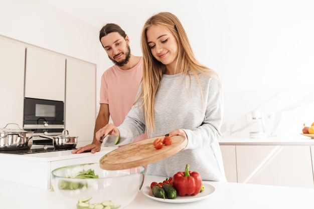 Vrolijk lief paar dat samen een gezonde maaltijd kookt terwijl ze in de keuken staan, met een snijplank met gesneden groenten