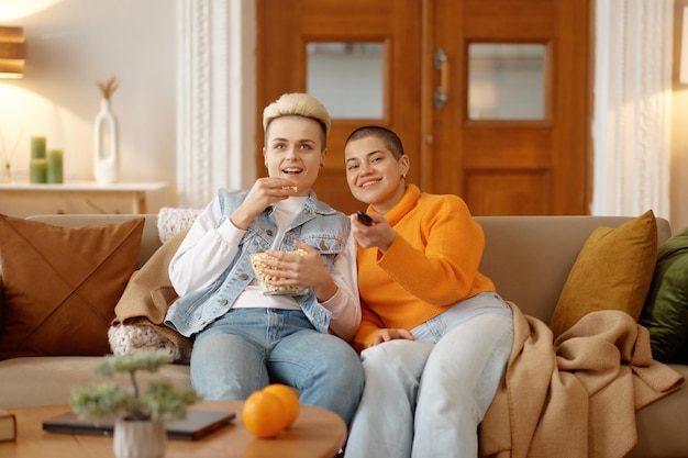 Vrolijk liefhebbend lesbisch vrouwenpaar dat popcorn eet en naar een film of tv-show kijkt in de huiskamer