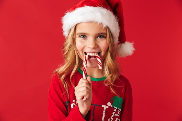 Vrolijk meisje dat Kerstmiskostuum draagt dat zich geïsoleerd bevindt, het suikergoed van het Kerstmissuikergoed eet