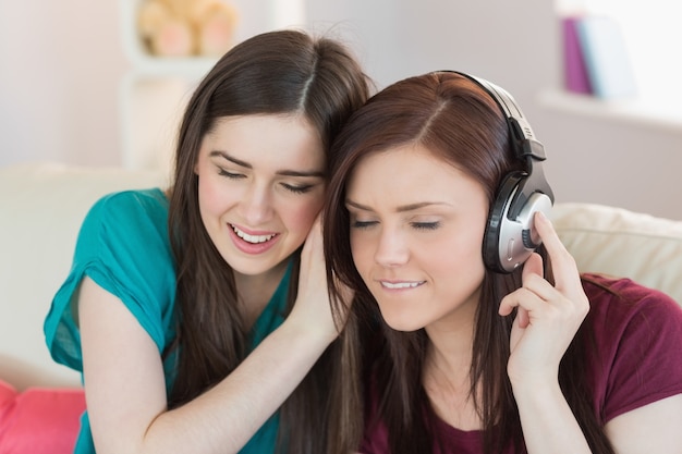 Vrolijk meisje die aan muziek met haar vriend naast haar op de bank luisteren