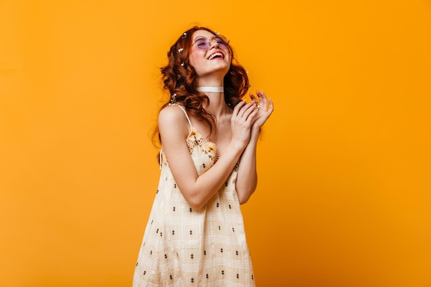 Vrolijk meisje in geruite jurk met bloemen lacht Portret van vrouw in lila bril op oranje achtergrond