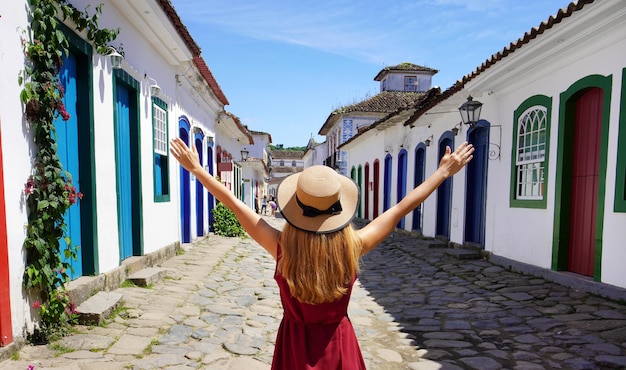 Vrolijk meisje in paraty brazilië mooie jonge vrouw met opgeheven armen wandelen in kleurrijke historische stad paraty unesco world heritage site brazilië