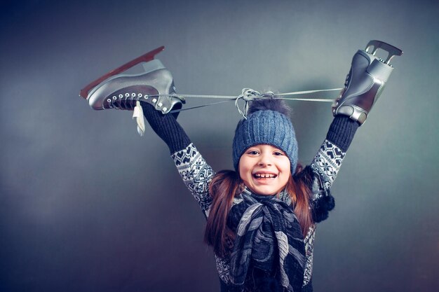 Vrolijk meisje in warme trui en muts met kunstschaatsen.