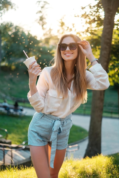 Vrolijk meisje in zonnebril die een milkshake drinkt en glimlacht