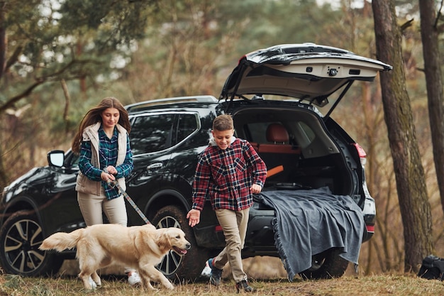 Vrolijk meisje met broer wandelen met hun hond buiten in het bos in de herfst of lente in de buurt van auto