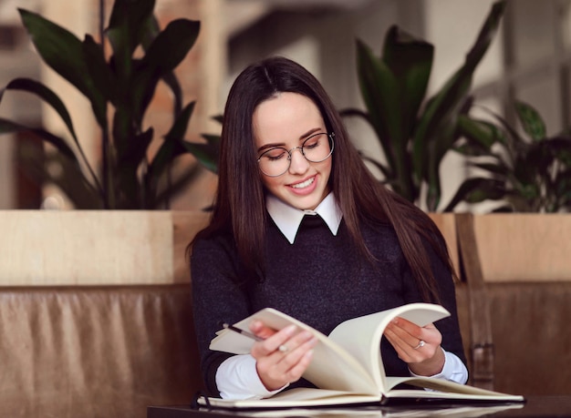 Vrolijk meisje met een bril bladert door een notitieboekje en zoekt er iets in