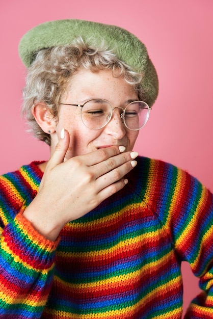 Vrolijk meisje met een regenboogtrui en een groene baret op een roze achtergrond