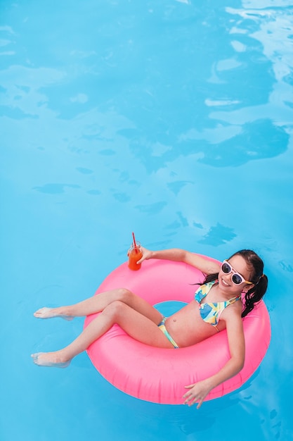 Vrolijk meisje met fruitdrank chillen op opblaasbare ring in zwembad