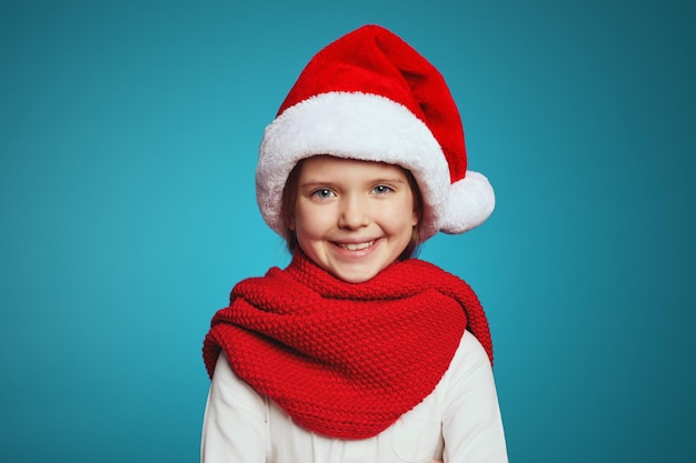 Vrolijk meisje met kerstmuts en rode sjaal die naar de camera kijkt