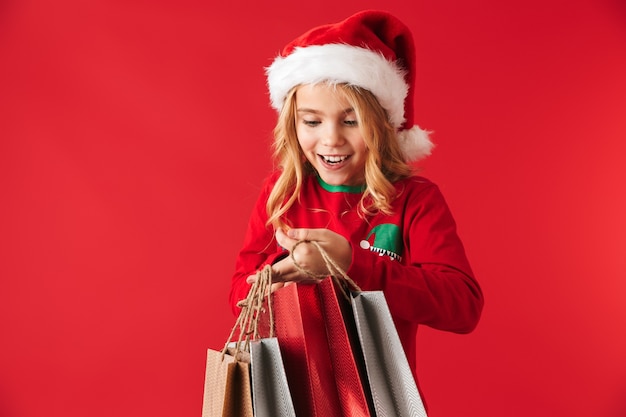 Vrolijk meisje met kerstmuts geïsoleerd staan, met boodschappentassen