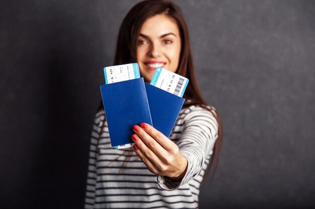 Vrolijk meisje met paspoort vliegticket voor grijze achtergrond indoor reisconcept