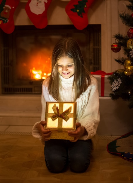 Vrolijk meisje openingsdoos met kerstcadeau. Lichte en glanzende glitters die uit de doos komen