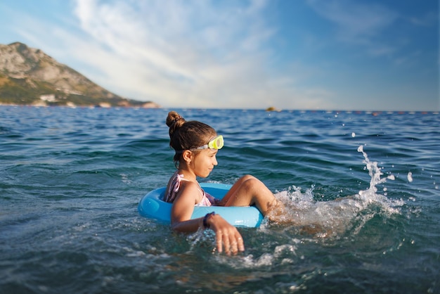 Vrolijk meisje zit in een opblaasbare cirkel en spettert met water in de zee