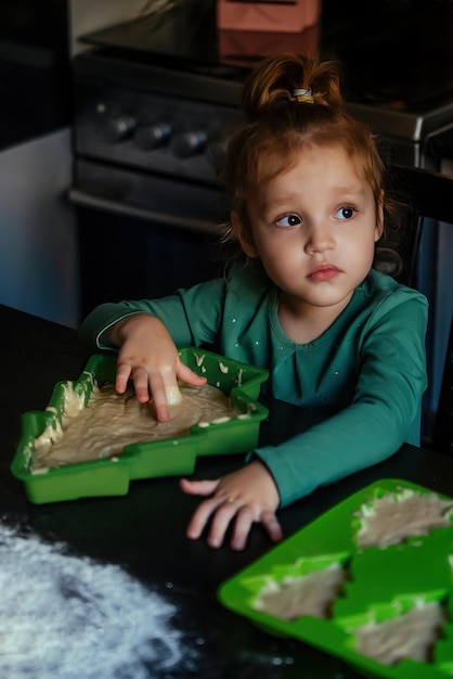 Vrolijk meisjesachtig thuis in de keuken die het deeg aanraakt voor eetbare kerstgebakjes