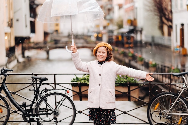 Vrolijk mooi meisje in een jas met een doorzichtige paraplu in Annecy. Frankrijk. Het meisje heft vrolijk een paraplu op in de regen.