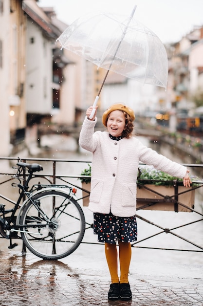 Vrolijk mooi meisje in een jas met een doorzichtige paraplu in Annecy