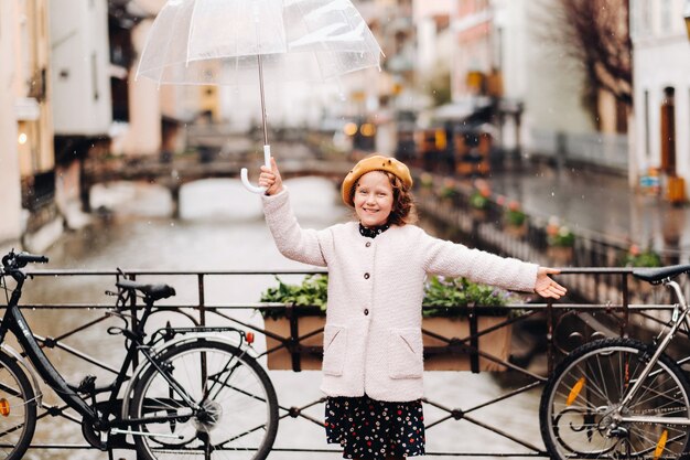 Vrolijk mooi meisje in een jas met een transparante paraplu in Annecy. Frankrijk. Het meisje heft vrolijk een paraplu op in de regen.