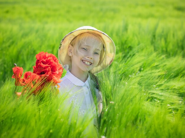 Vrolijk mooi meisje met een boeket van papavers op een gebied van groene rogge.