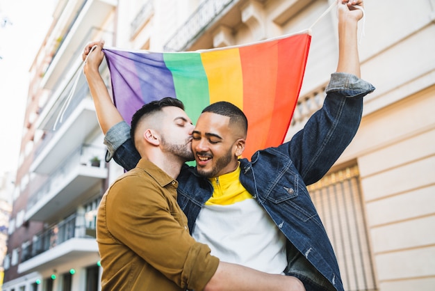 Foto vrolijk paar dat en hun liefde met regenboogvlag omhelst toont.