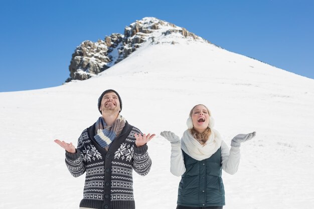 Vrolijk paar met open handen het kijken omhoog voor gesneeuwde heuvel