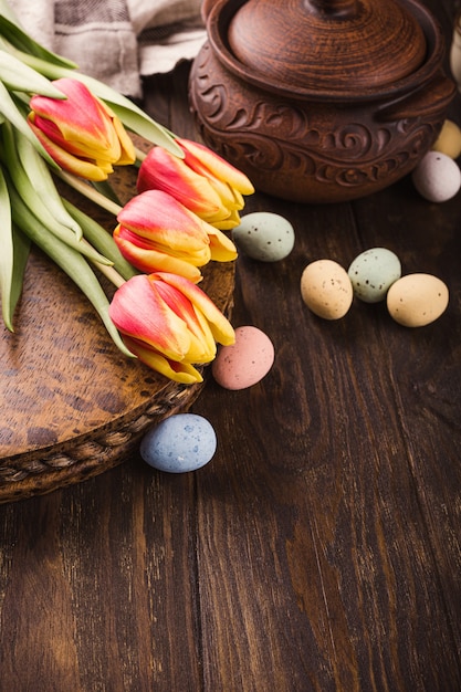 Vrolijk Pasen-oppervlak met tulpen en kleurrijke kwarteleitjes in metalen mand op houten oppervlak. Kopieer ruimte