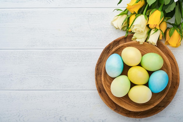 Vrolijk Pasen Paaseieren op rustieke tafel met witte en gele rozen Natuurlijk geverfde kleurrijke eieren in houten plaat en lentebloemen in rustieke kamer Getinte afbeelding Pasen achtergrond met kopie ruimte