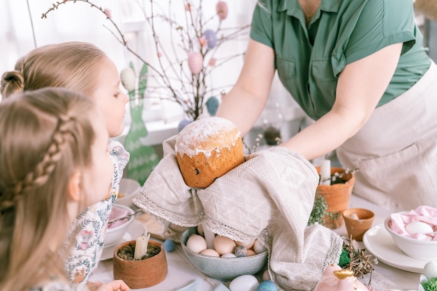 Vrolijk pasen vakantie tijd in lente seizoen familie jongen meisjes kinderen zussen en jonge vrouw houdt gebakken gebak cake of traditioneel brood in haar handen traditionele handgemaakte gerechten feestelijke interieur