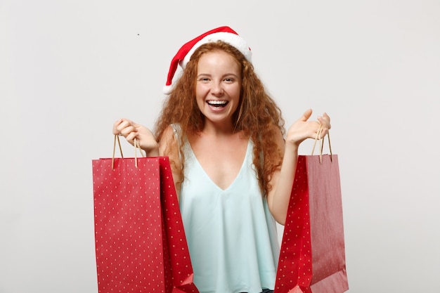 Vrolijk roodharige Santa meisje in kerstmuts geïsoleerd op een witte achtergrond. Gelukkig Nieuwjaar 2020 viering vakantie concept. Bespotten kopie ruimte. Houd de pakkettas met geschenken of aankopen vast na het winkelen.