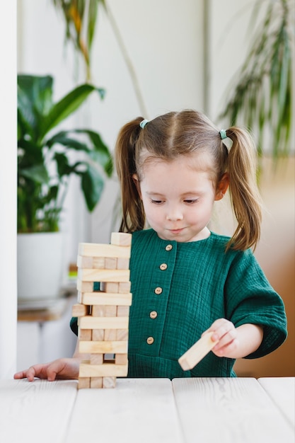 Vrolijk schattig klein meisje met paardenstaarten die een houten blok uit een jenga-toren trekken Binnenactiviteiten