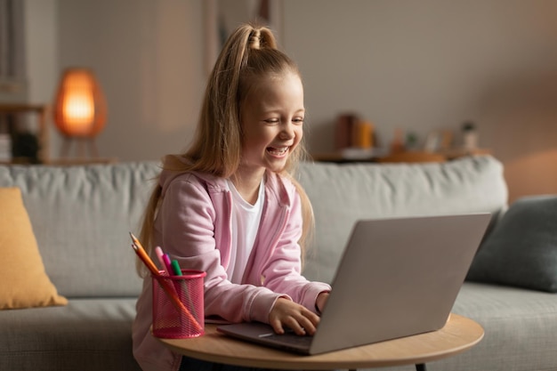 Vrolijk schoolmeisje met behulp van laptopcomputer surfen op internet om thuis te zitten