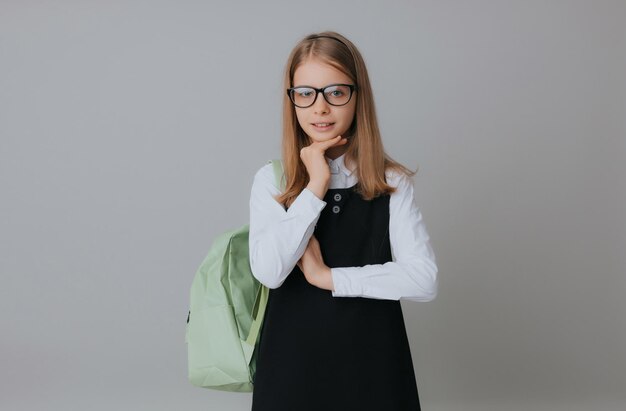 Vrolijk tienermeisje 111213 jaar oud in een schooluniform draagt een rugzak op een grijze achtergrond schoolmode