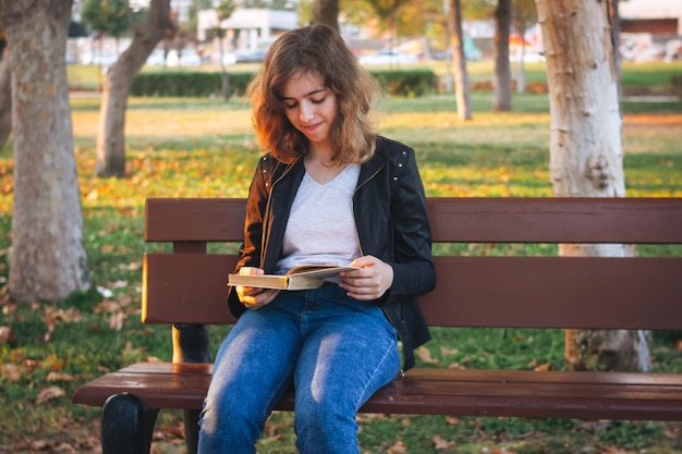 Vrolijk tienermeisje dat een boek leest op de bank in het herfstpark