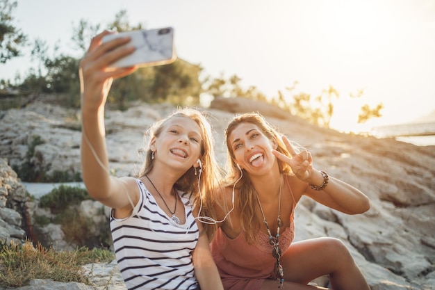 Vrolijk tienermeisje en haar jonge moeder die plezier hebben en een selfie maken terwijl ze genieten van een zomervakantie op een zee-rotsstrand.