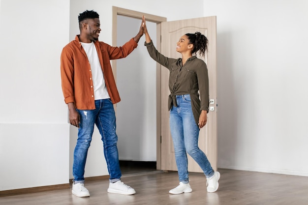 Foto vrolijk zwart stel geeft high five terwijl ze in nieuw huis staan