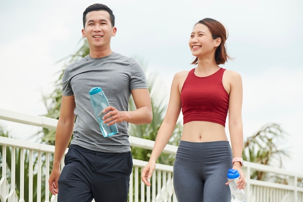 Vrolijk zweterig jong Aziatisch stel dat buiten loopt en vers water drinkt na de training