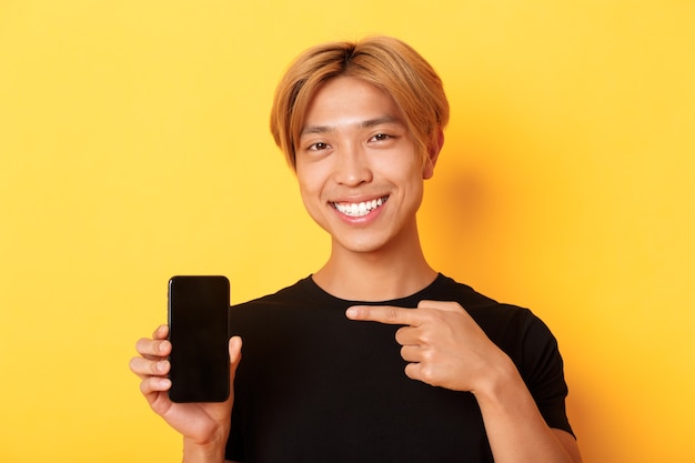 Vrolijke aantrekkelijke Koreaanse man wijzende vinger op het scherm van de mobiele telefoon