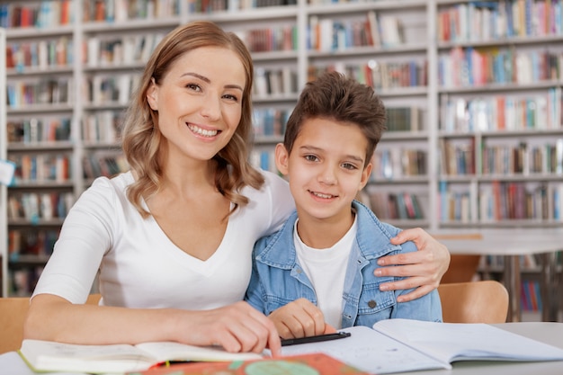 Vrolijke aantrekkelijke vrouw en haar charmante jonge zoon glimlachen, die bij de bibliotheek bestuderen