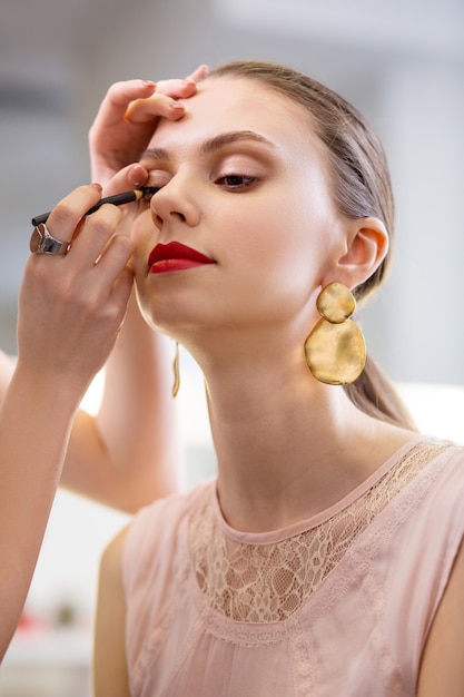 Vrolijke aardige vrouw die haar make-up laat doen door een visagiste terwijl ze er mooi uit wil zien