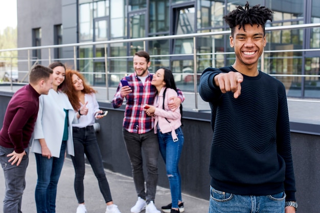 Foto vrolijke afrikaanse mens die naar camera richt die zich voor zijn vrienden bevindt