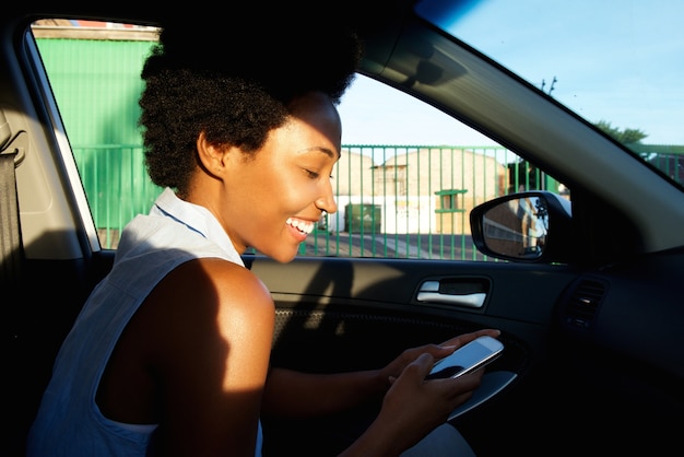 Vrolijke Afrikaanse vrouw die mobiele telefoon in een auto met behulp van