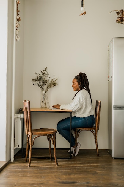 Vrolijke afro-amerikaanse vrouw die laptop gebruikt terwijl ze op een stoel zit in de woonkamer verticale kopie spa