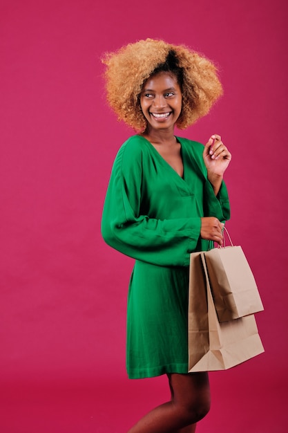 Vrolijke afro-vrouw die bruine papieren boodschappentassen vasthoudt terwijl ze over een geïsoleerde achtergrond staat.