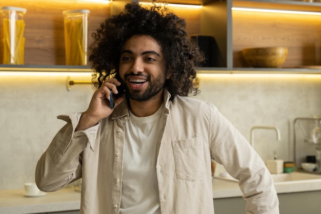 Vrolijke Arabische man praat aan de telefoon met een vriend in de keuken