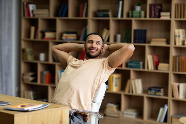 Vrolijke arabische mannelijke freelancer die achterover leunt op een stoel die ontspant na succesvol werk aan een bureau met laptop