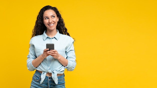 Vrolijke Arabische vrouw met behulp van mobiele telefoon op gele achtergrond Panorama