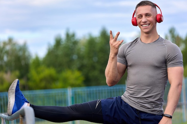 Vrolijke atleet glimlacht terwijl hij zijn benen strekt terwijl hij naar muziek luistert met een koptelefoon