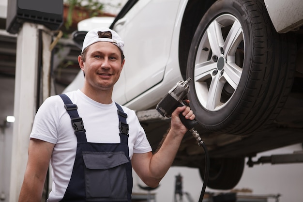 Vrolijke autoservicemedewerker met elektrische momentsleutel, werkend in de garage