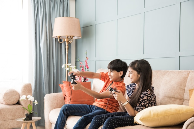 Vrolijke Aziatische Indiase kinderen spelen videogame met controller of joystick, zittend op de bank, bank