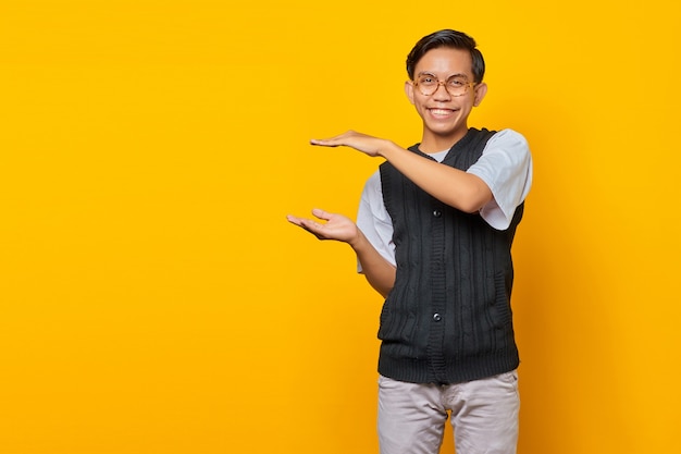 Vrolijke Aziatische man die product over gele achtergrond toont