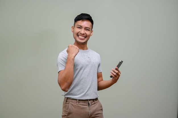 Vrolijke Aziatische man met duim omhoog handgebaar terwijl hij zijn telefoon vasthoudt en naar de camera glimlacht